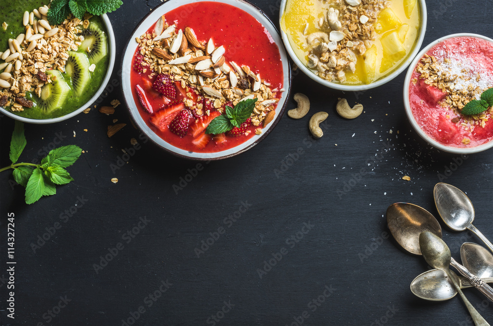 健康的夏季早餐概念。彩色水果奶昔碗，黑b上有坚果和燕麦格兰诺拉麦片