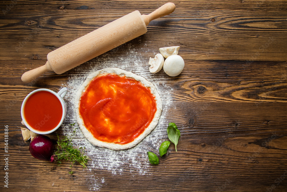 Pizza dough with tomato sauce on wooden table