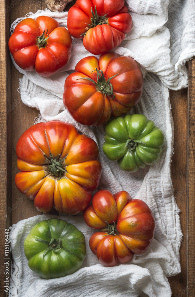 Colorful Heirloom tomatoes on white textile in rustic wooden tray, top view