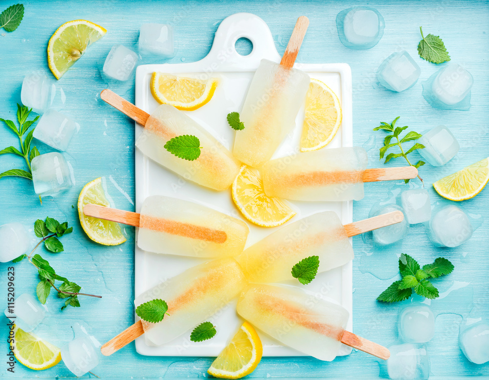 Lemonade popsicles with lemon slices, fresh mint leaves and ice cubes on white ceramic board