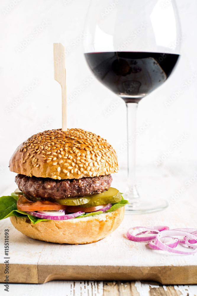 新鲜的自制汉堡，放在白木板上，配洋葱圈和一杯红酒。