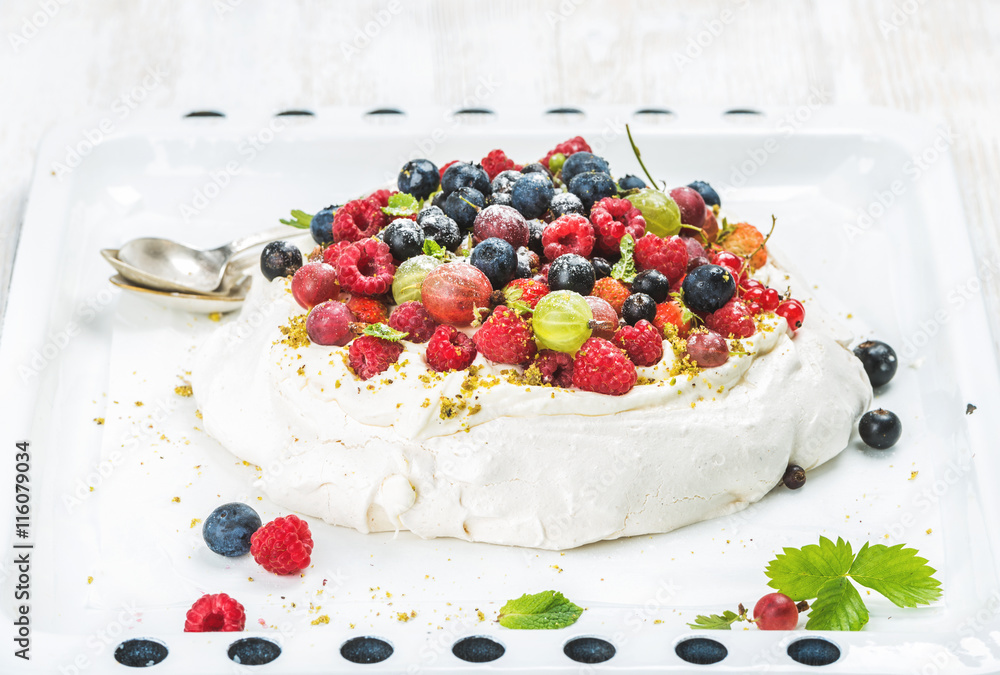Homemade Pavlova cake with fresh garden and forest berries on white baking tray over light wooden ba