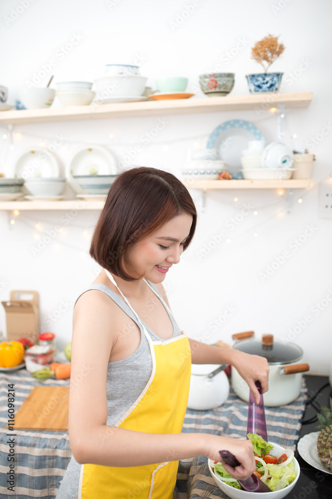 年轻的亚洲女人在厨房里做沙拉，面带微笑