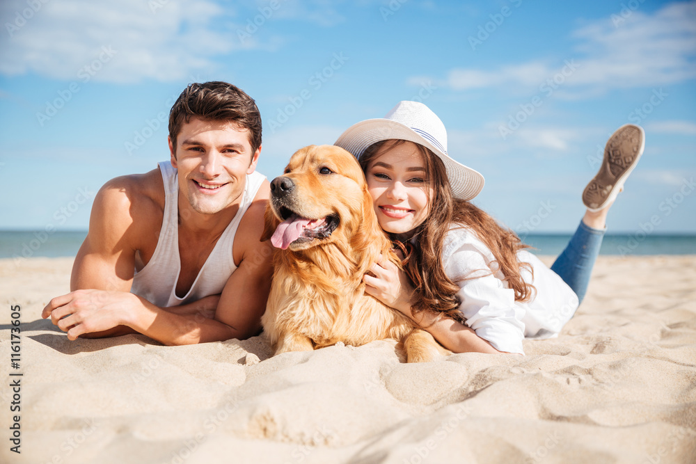 快乐的年轻情侣在海滩上与狗拥抱