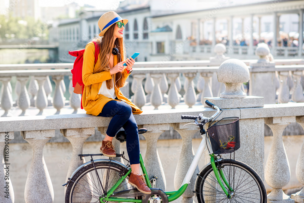 年轻的女旅行者骑着自行车坐在卢布尔雅那的三桥上使用智能手机。