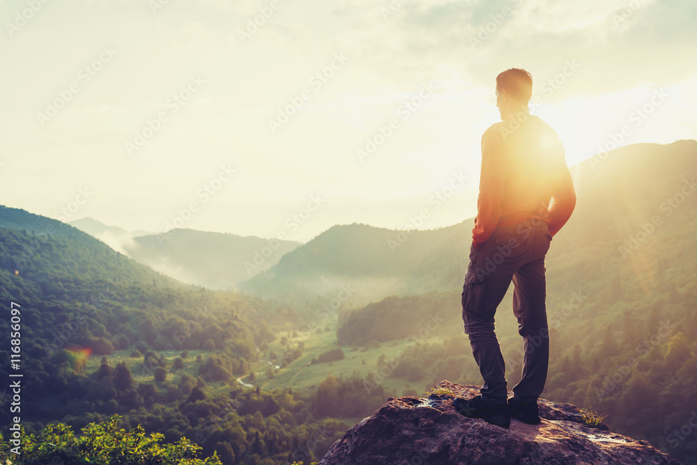 旅行者年轻人日落时站在夏日的群山中欣赏大自然