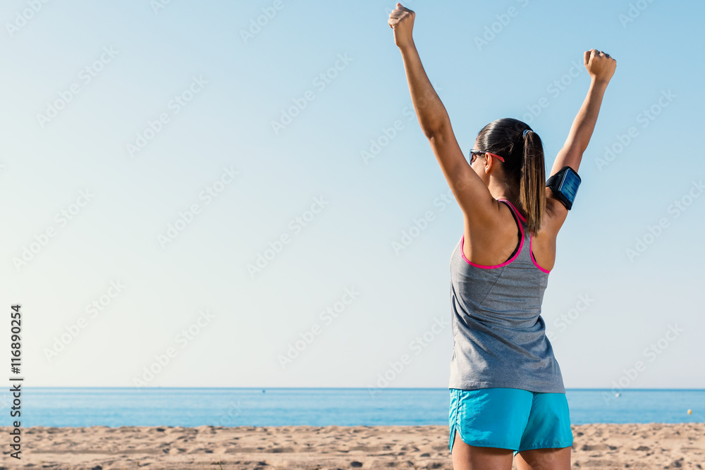 Woman athlete raising arms at sea.