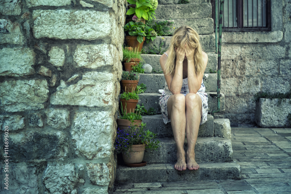一个悲伤的孤独女人坐在城市街道的石楼梯上，哭着捂住脸。