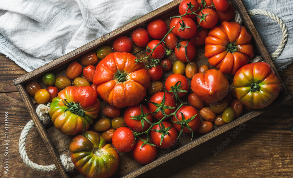 不同大小和种类的五颜六色的西红柿放在浅色纺织品和乡村风格的深色木托盘里