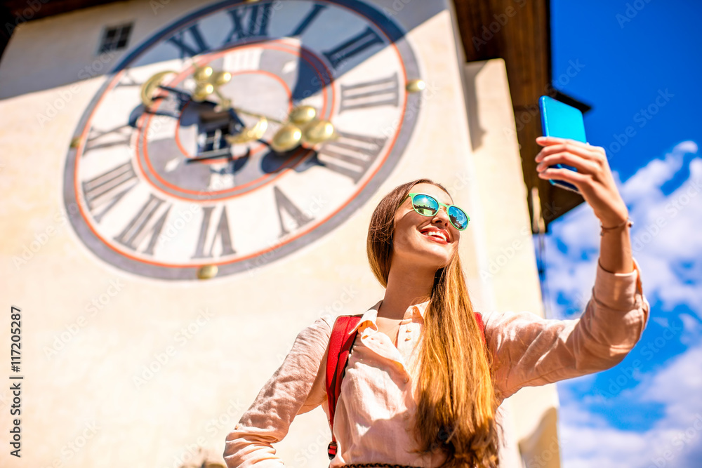 Young female traveler making selfie photo with smart phone on the old clock tower background in Graz