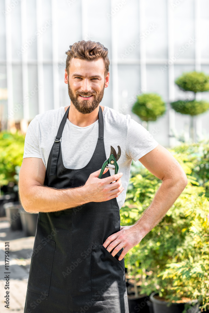 Portrait of a handsome gardener dressed in apron with scissors in the greenhouse.