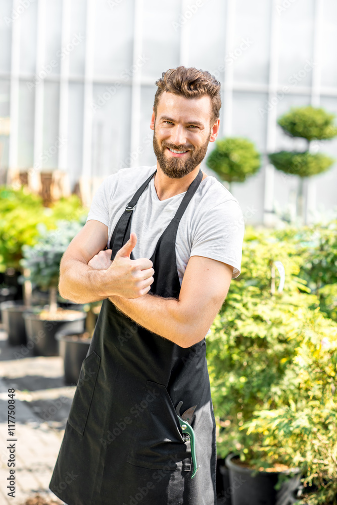 Portrait of a handsome gardener dressed in apron with scissors in the greenhouse.