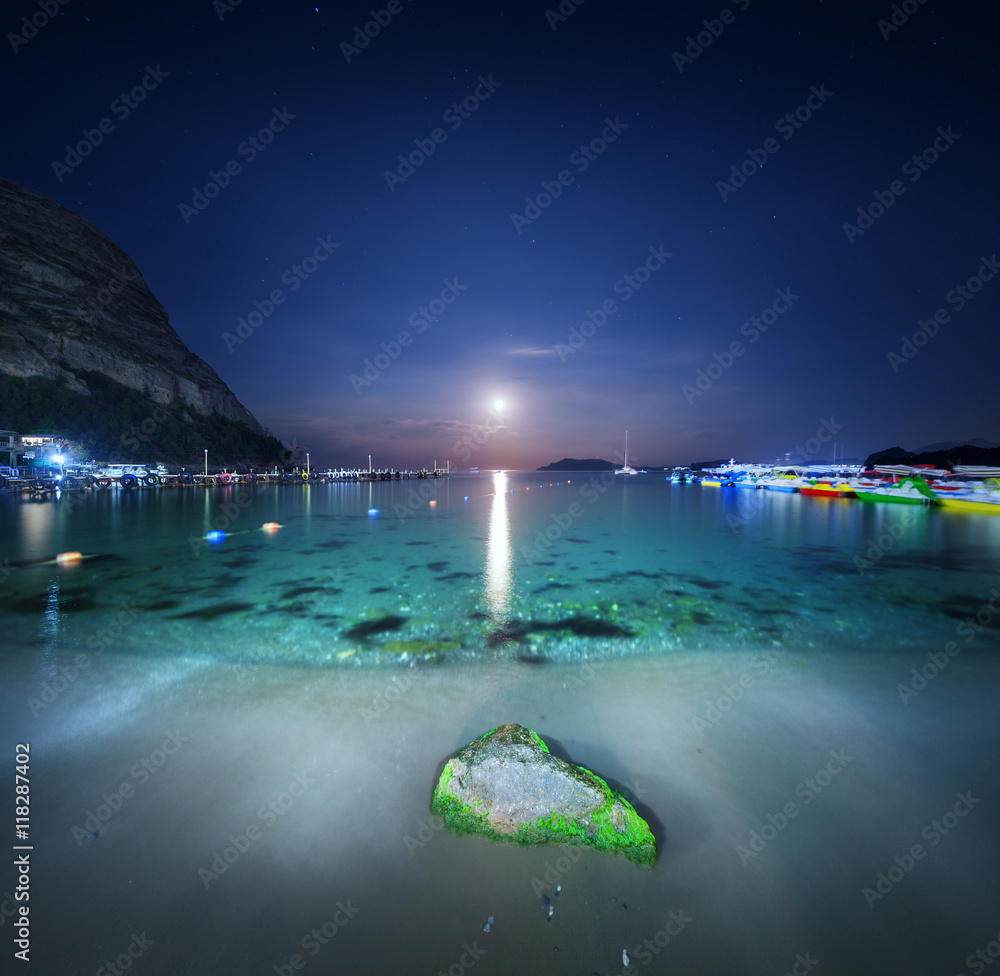 Night landscape at the sea with stone, yellow sand and lunar path. Moonrise. Travel background