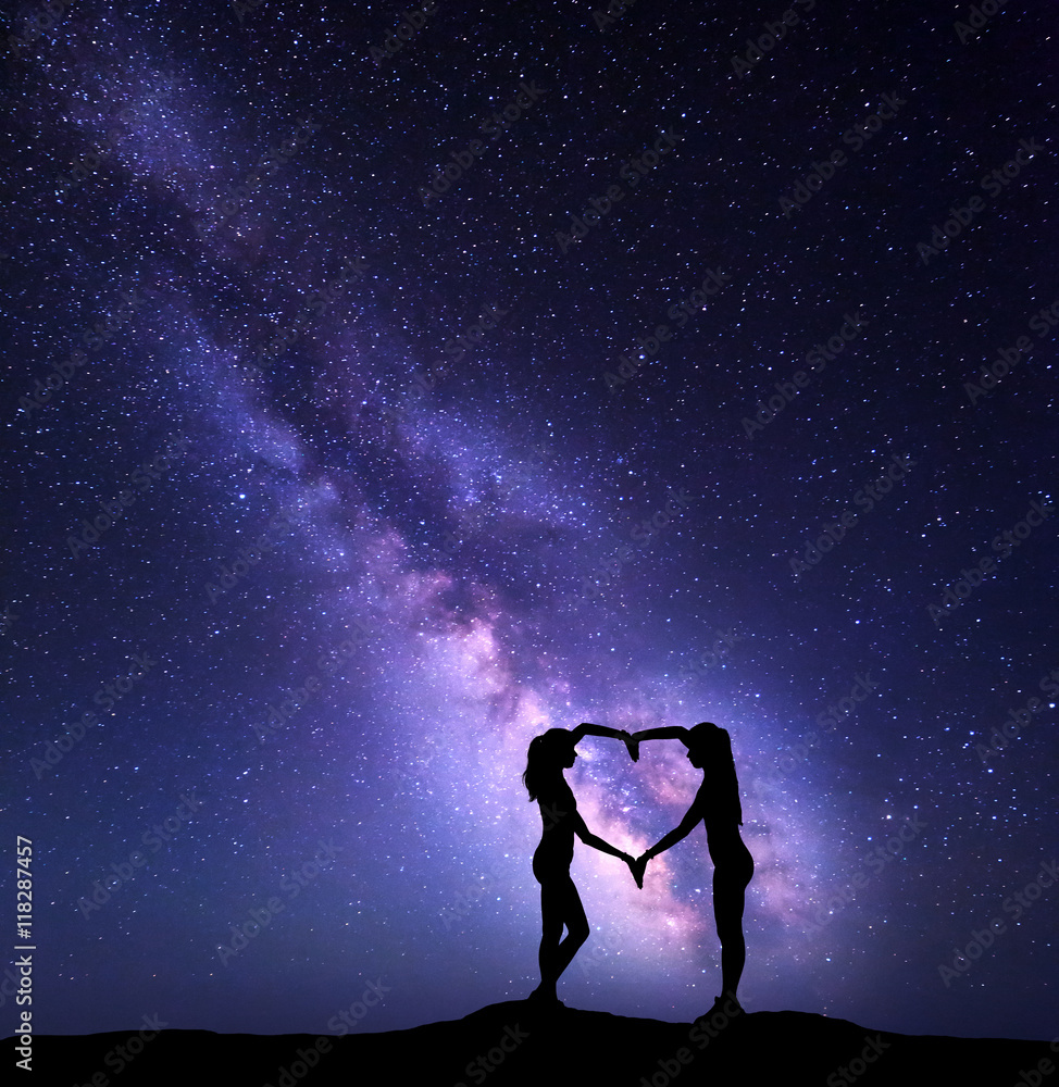 Girls holding hands in heart shape on the background of the colorful Milky Way. Night landscape with