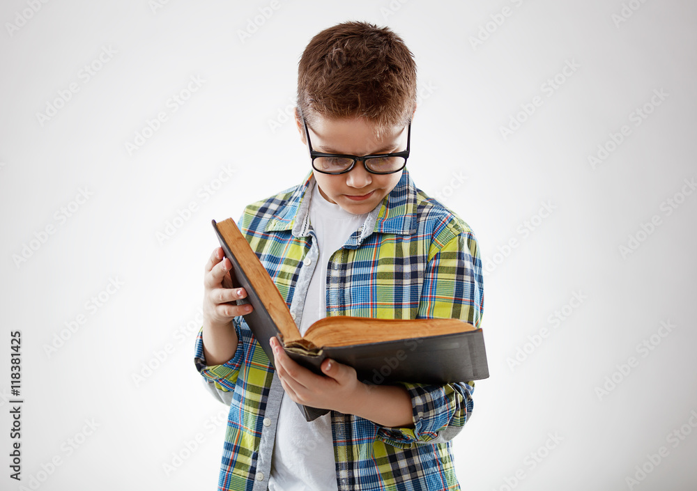 戴眼镜的少年儿童在灰色背景下翻书