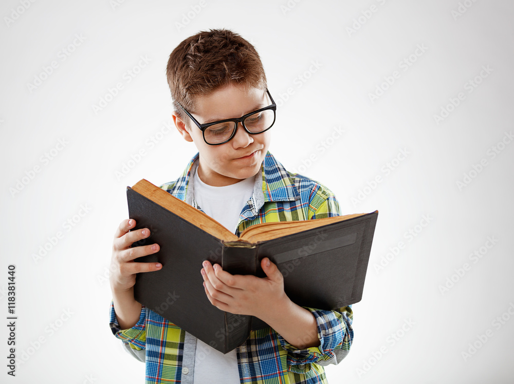 戴眼镜的少年儿童在灰色背景下翻书
