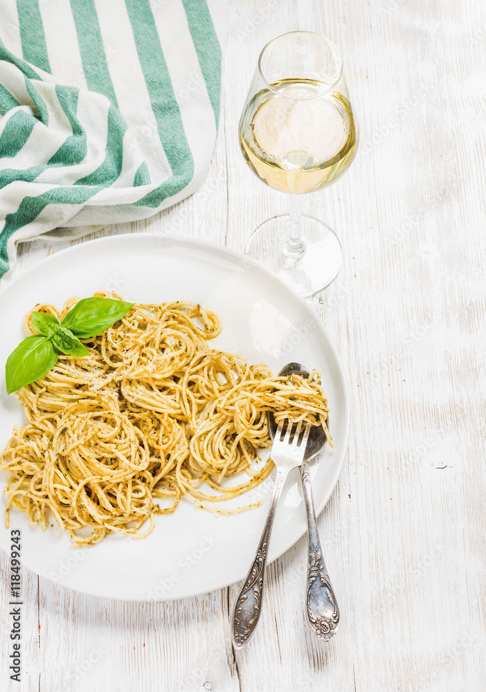 Pasta spaghetti with Pesto sauce and fresh basil, glass of white wine. White wooden painted backgrou