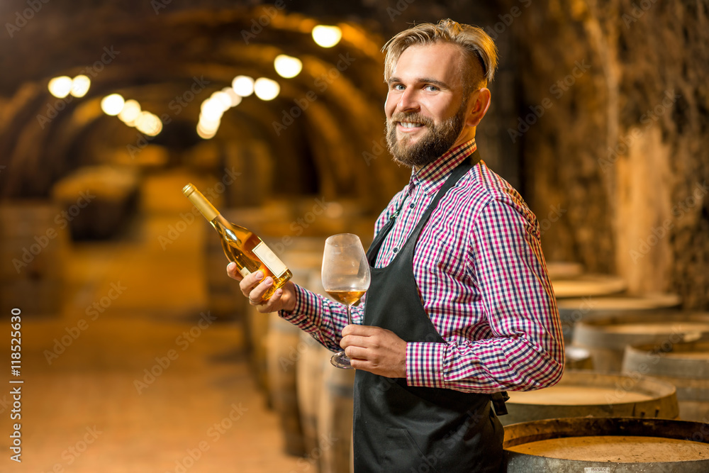一位英俊的侍酒师的肖像，他穿着围裙和格子衬衫，手里拿着酒瓶，站在旧c里