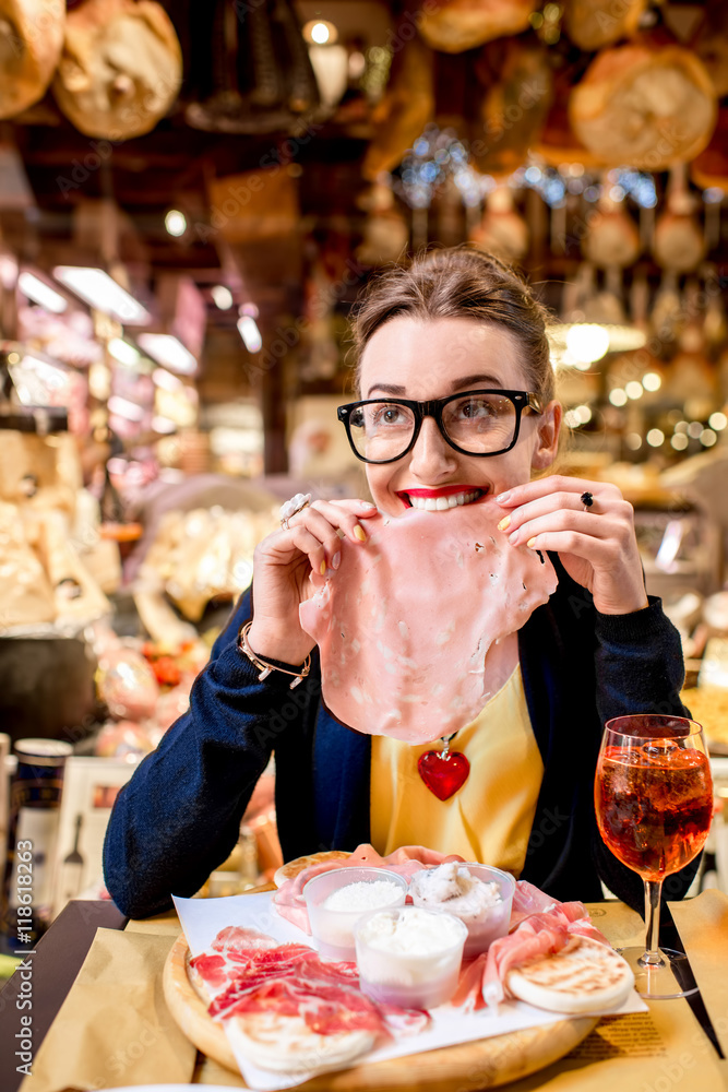 Young woman with big slice of mortadella sausage in front of food showcase in Bologna city. Mortadel