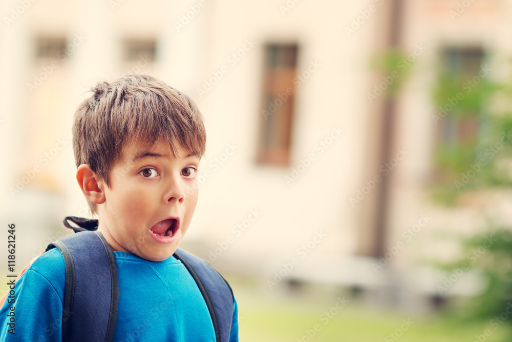 男孩背着帆布背包在学校大楼前。孩子背着背包