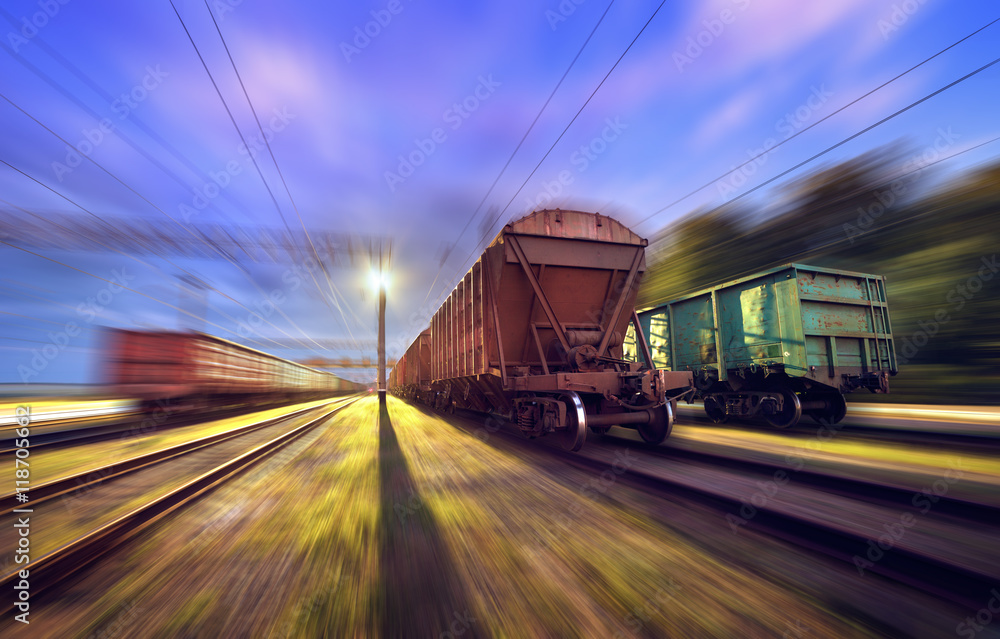 Railway station with cargo wagons in motion at night. Railroad with motion blur effect. Heavy indust