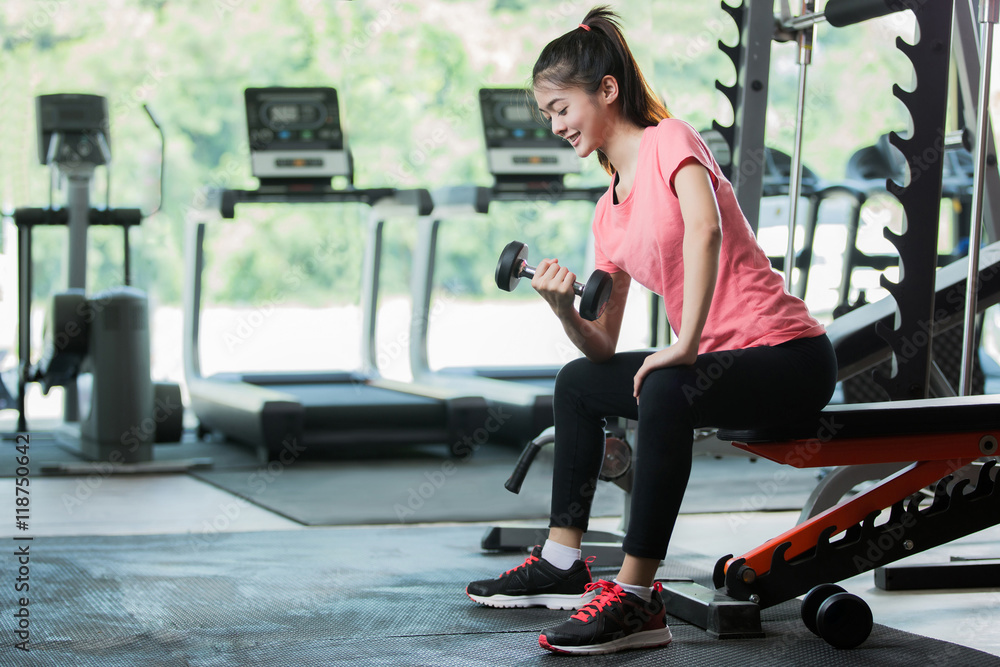 亚洲女性在健身房举哑铃锻炼。