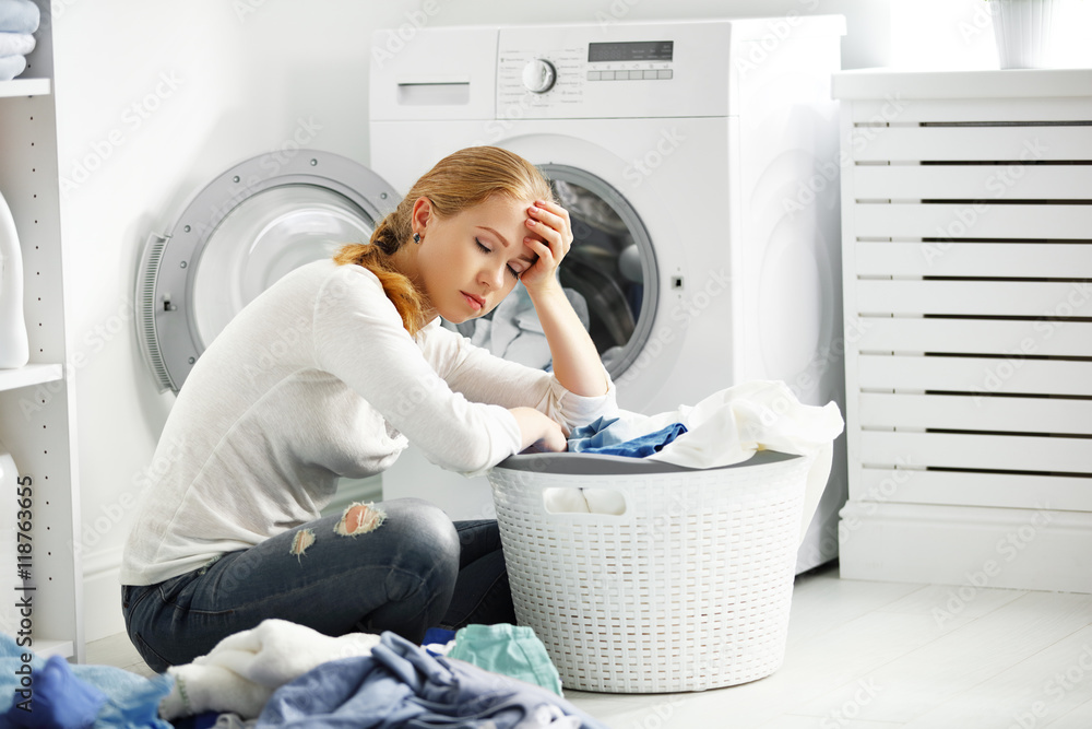 疲惫不快乐的女人家庭主妇把衣服叠到洗衣机里