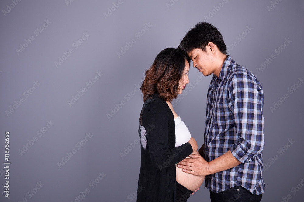 年轻夫妇：灰色背景下怀孕的母亲和幸福的父亲
