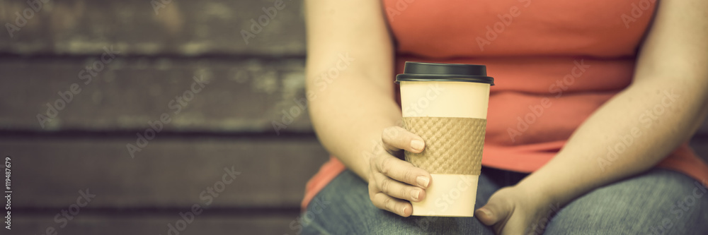 坐在木长椅上拿外卖咖啡的女人