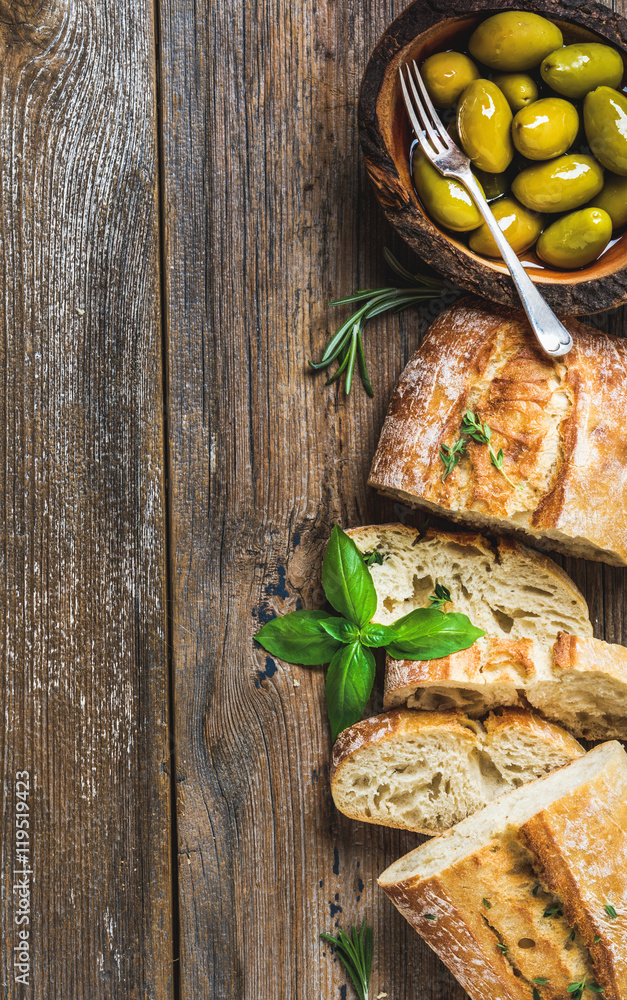 碗里的绿色地中海橄榄和乡村木质背景上的新鲜烤ciabatta片