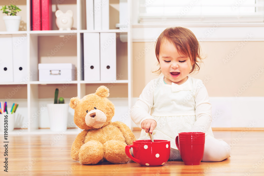 蹒跚学步的女孩和她的泰迪熊一起喝茶