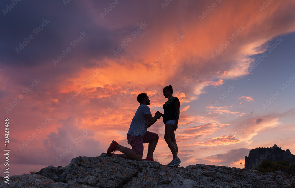 山峰上一名男子向女友求婚的剪影景观