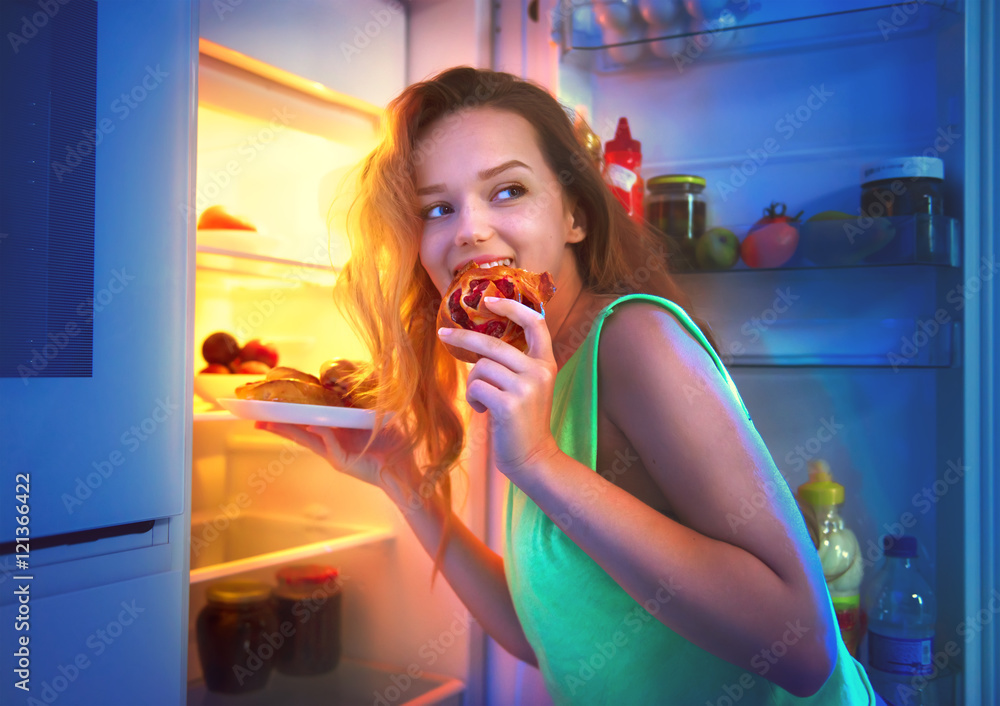 美丽的少女晚上从冰箱里拿食物