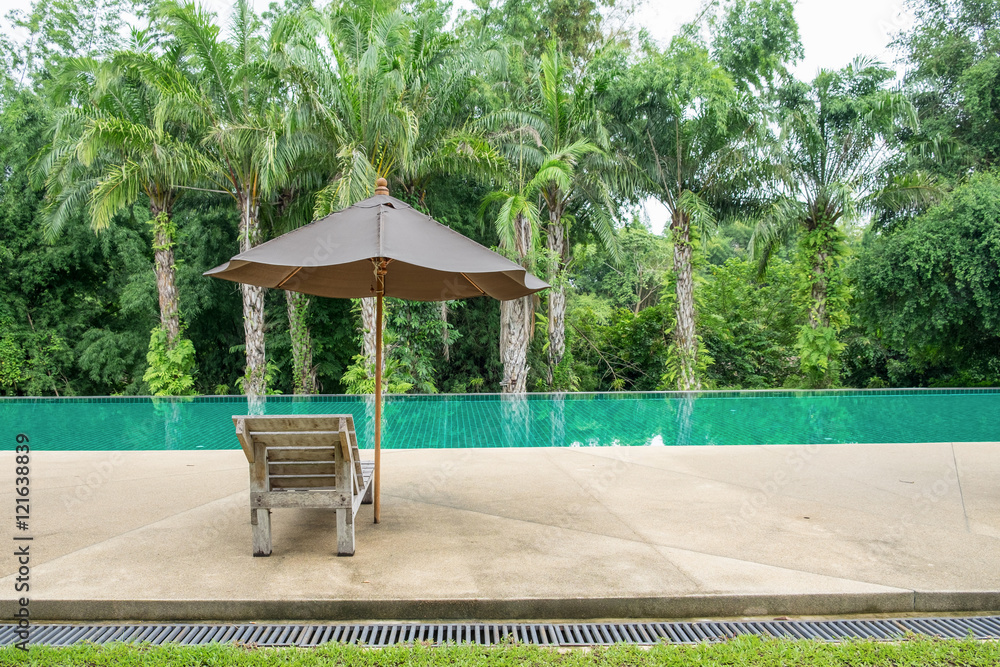 阴凉花园现代游泳池上带伞的木制日光浴床