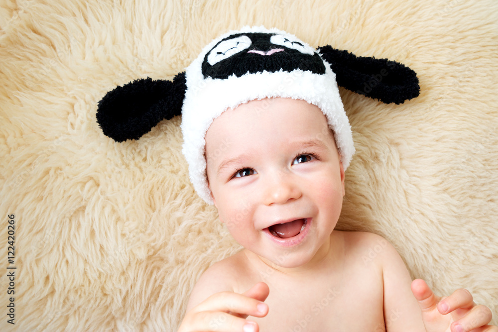 一岁婴儿戴着羊帽子躺在羊毛上