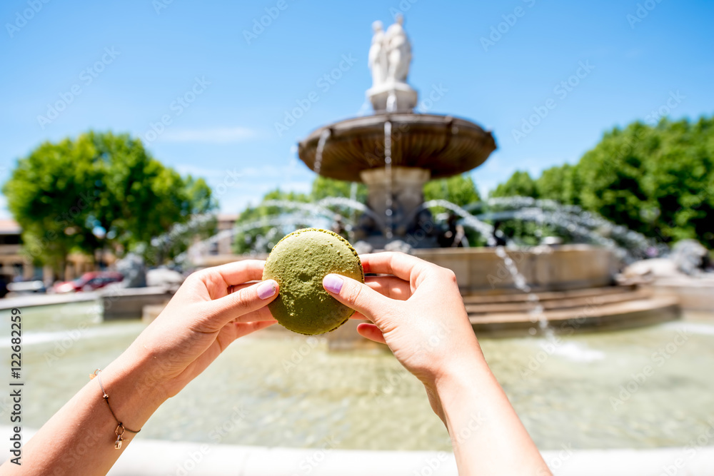 Female hands holding macaron cookie near the famous fontain de la Rotonde in Aix-en-Provence in Fran