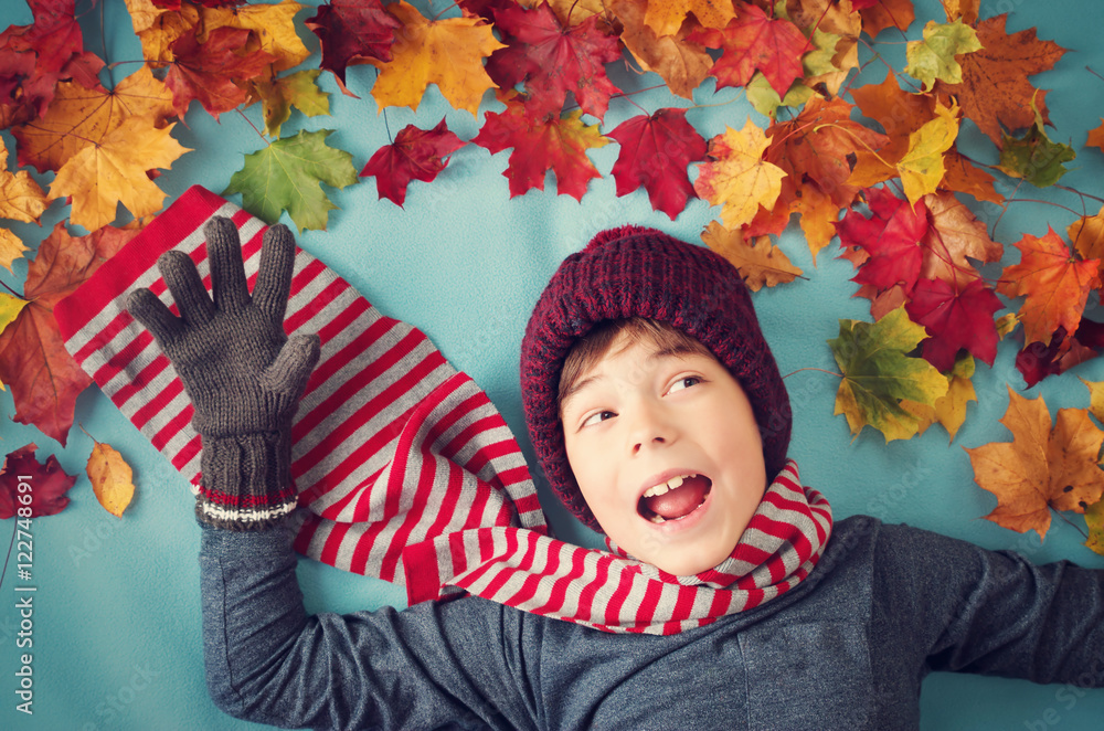 七岁男孩在秋天做梦。戴帽子、戴围巾、蓝底枫叶的孩子