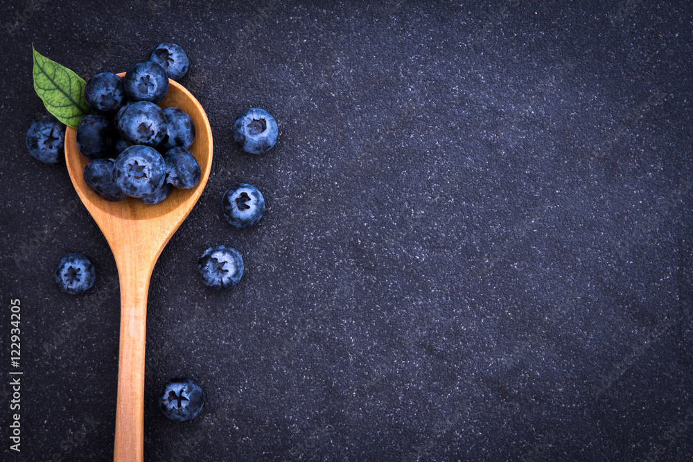 黑石头背景的木勺里新鲜采摘的蓝莓