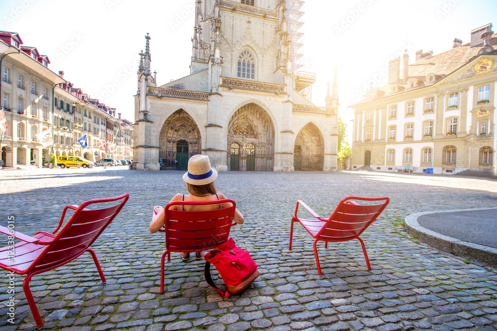 年轻的女游客坐在伯尔尼老城明斯特广场的红色公共椅子上