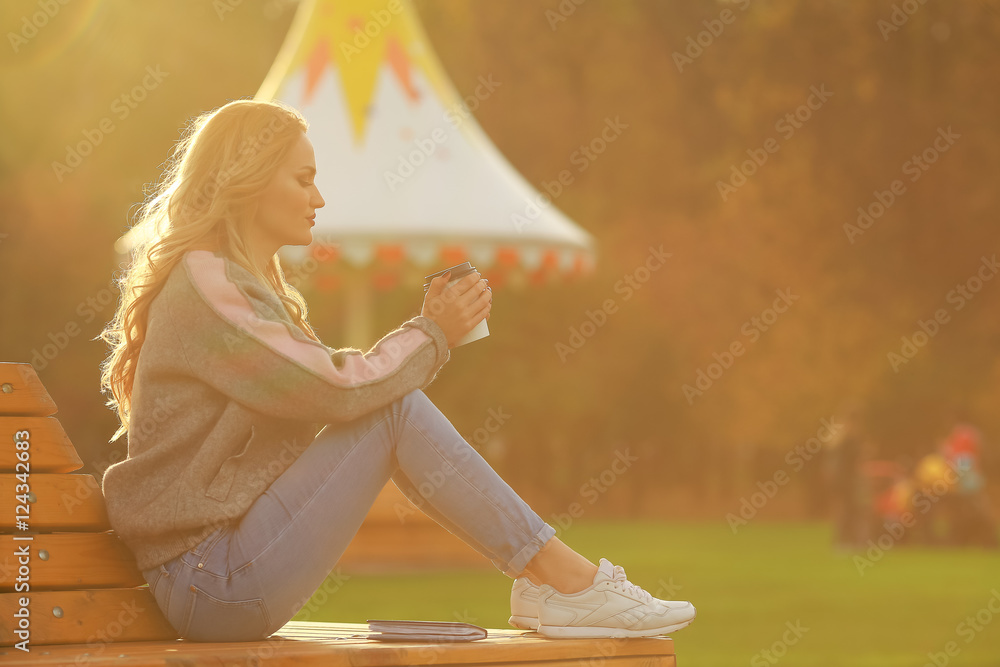 年轻时尚的女人在公园里喝咖啡。日落时的美丽女孩。