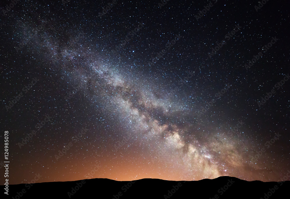 夜空中有令人惊叹的银河系和山上的黄光。星空中有山丘