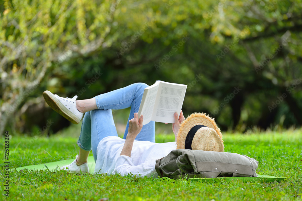 快乐的女人躺在绿草上在公园里看书（户外）