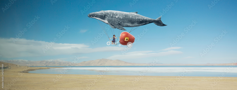 旅行理念。鲸鱼漂浮在天空中，用梦幻苹果自行车载着一个快乐的妹妹。