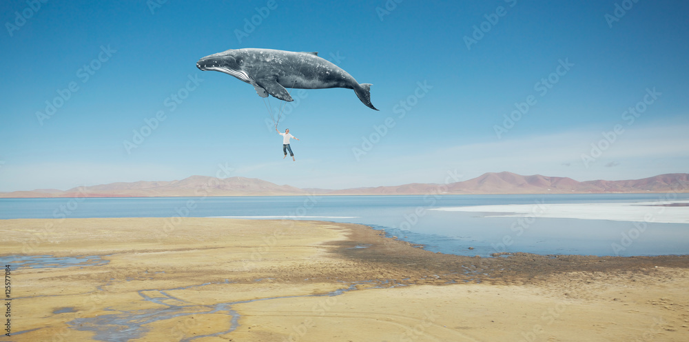 旅行理念。鲸鱼漂浮在空中，载着一个快乐的亚洲年轻人。