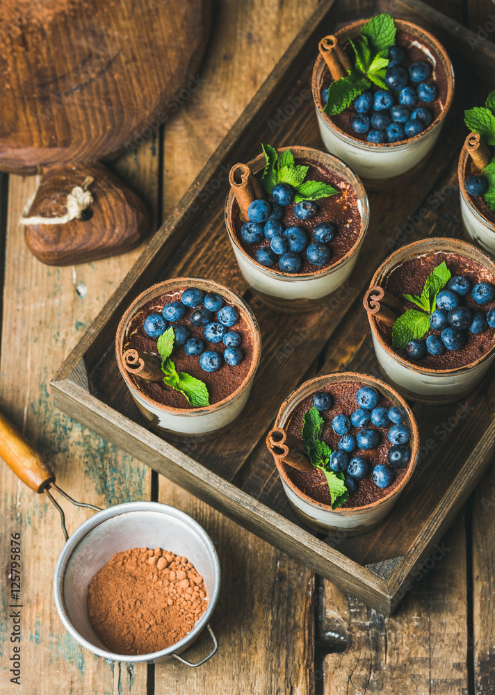 自制提拉米苏甜点，装在玻璃杯里，肉桂、薄荷和新鲜蓝莓放在木托盘里，还有si