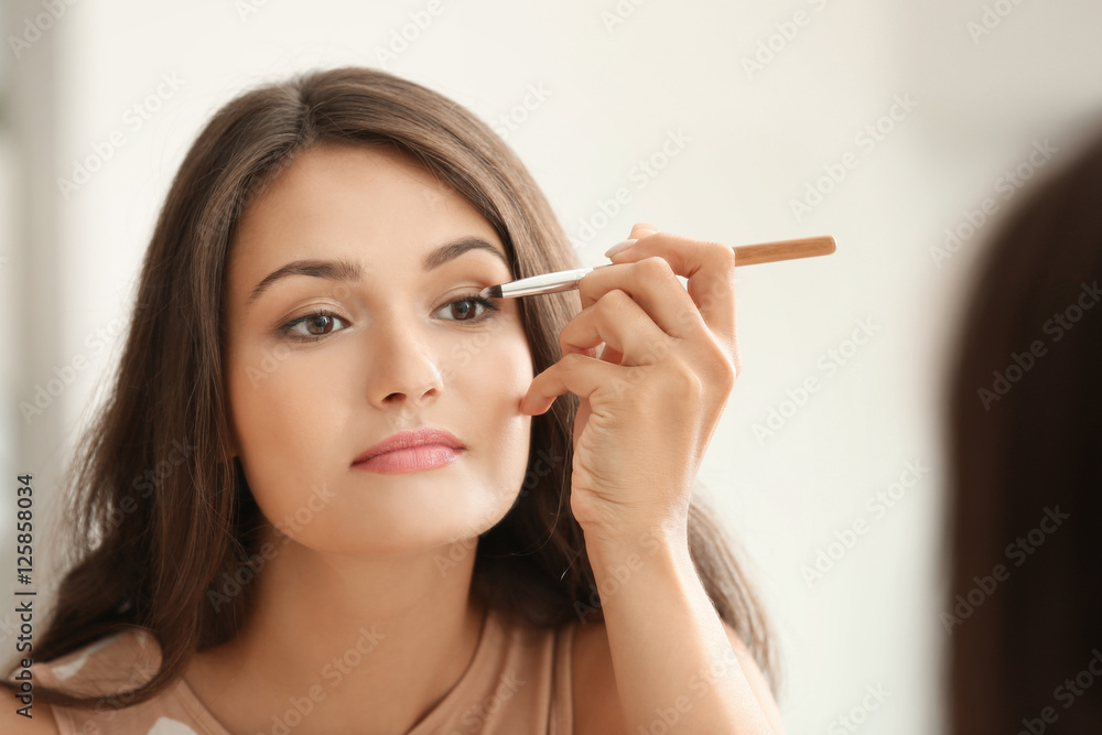 Beautiful girl applying cosmetics in front of mirror