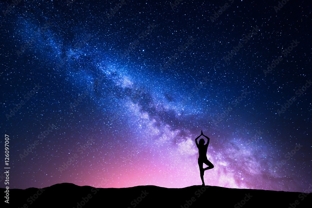 银河系，一个站着的女人在山上练习瑜伽的剪影。美丽的风景w