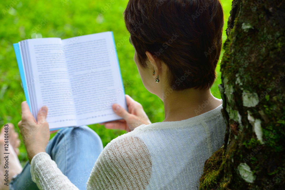 一位中年妇女坐在公园的树下看书