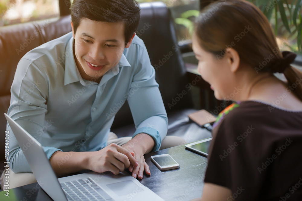 Young Asian businessman and woman meeting in coffee shop, using laptop for presentation