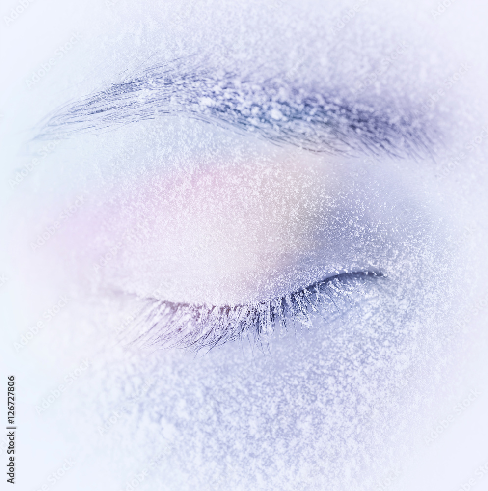 冬天浅蓝色背景下，睫毛上有霜或雪的闭眼微距特写。Gent